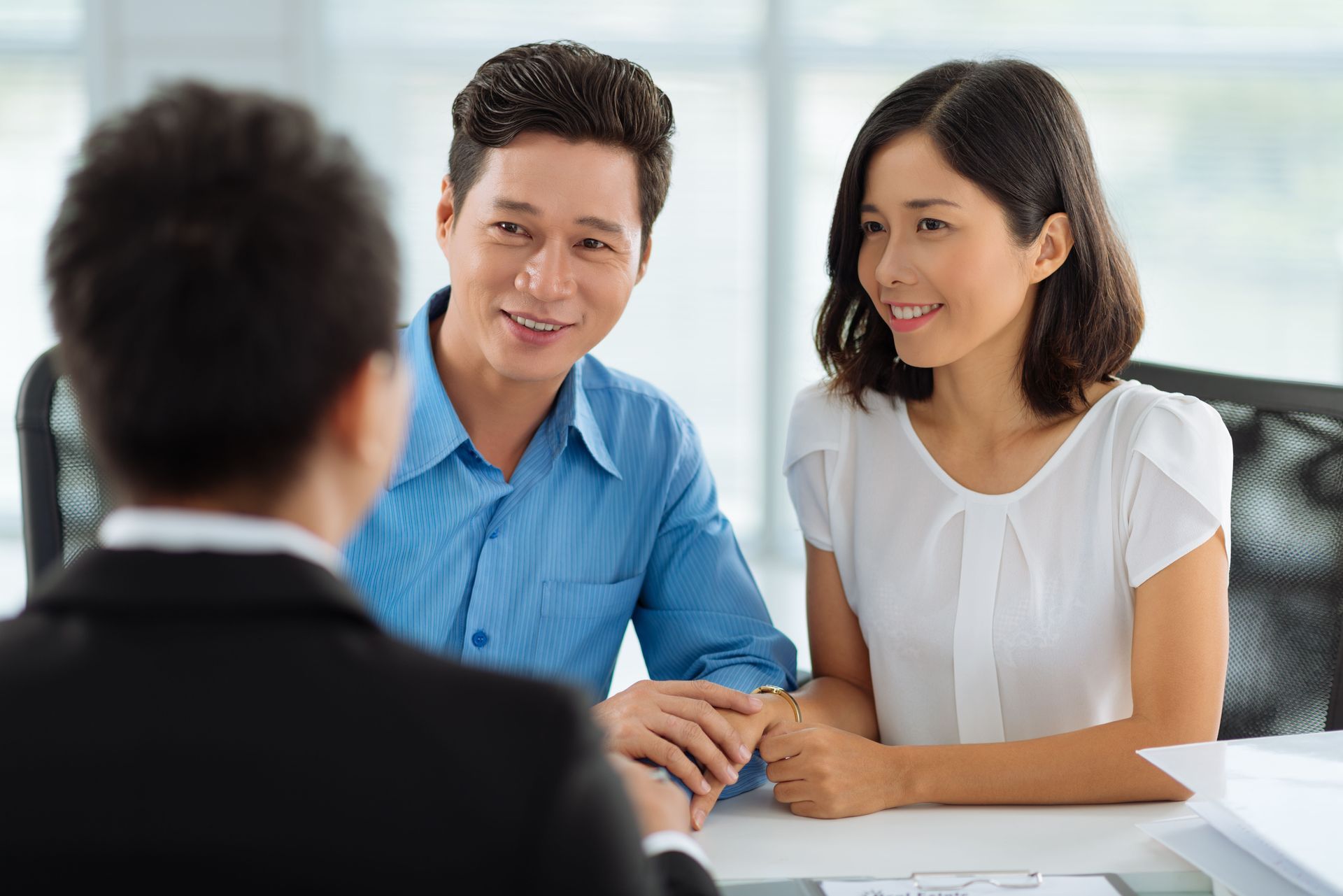 Couple smiling at person in a suit, possibly meeting with financial advisor in an office.