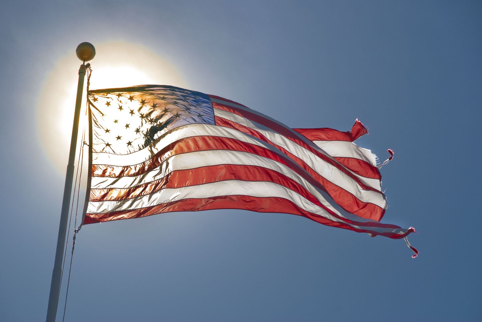 American flag waving in the sunlight against a clear blue sky.