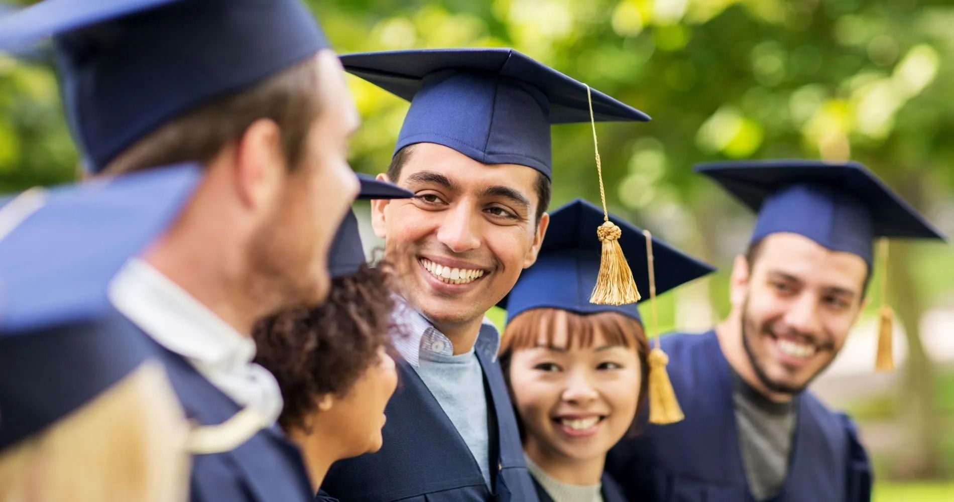 Graduates in blue caps and gowns smiling outdoors.