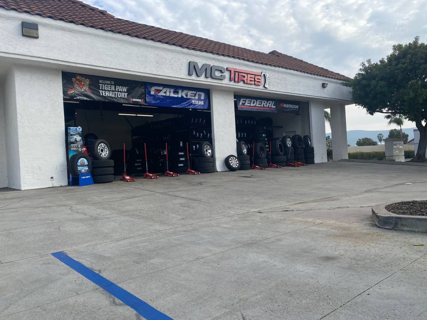 MC Tires shop exterior, tires displayed, blue signage, overcast sky.