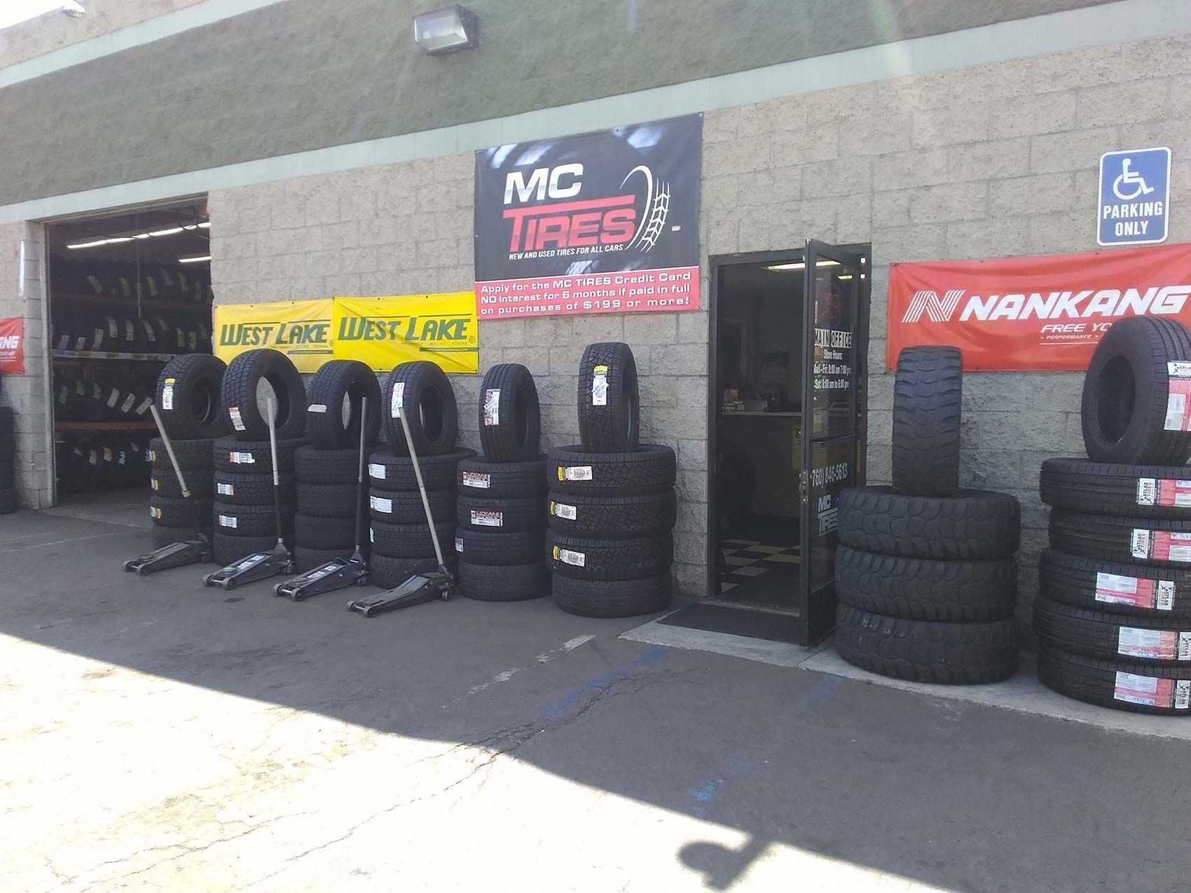 MC Tires shop exterior; tires stacked outside, doorway, banners.