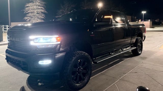 Black Ram pickup truck parked on pavement at night, headlights and fog lights on.