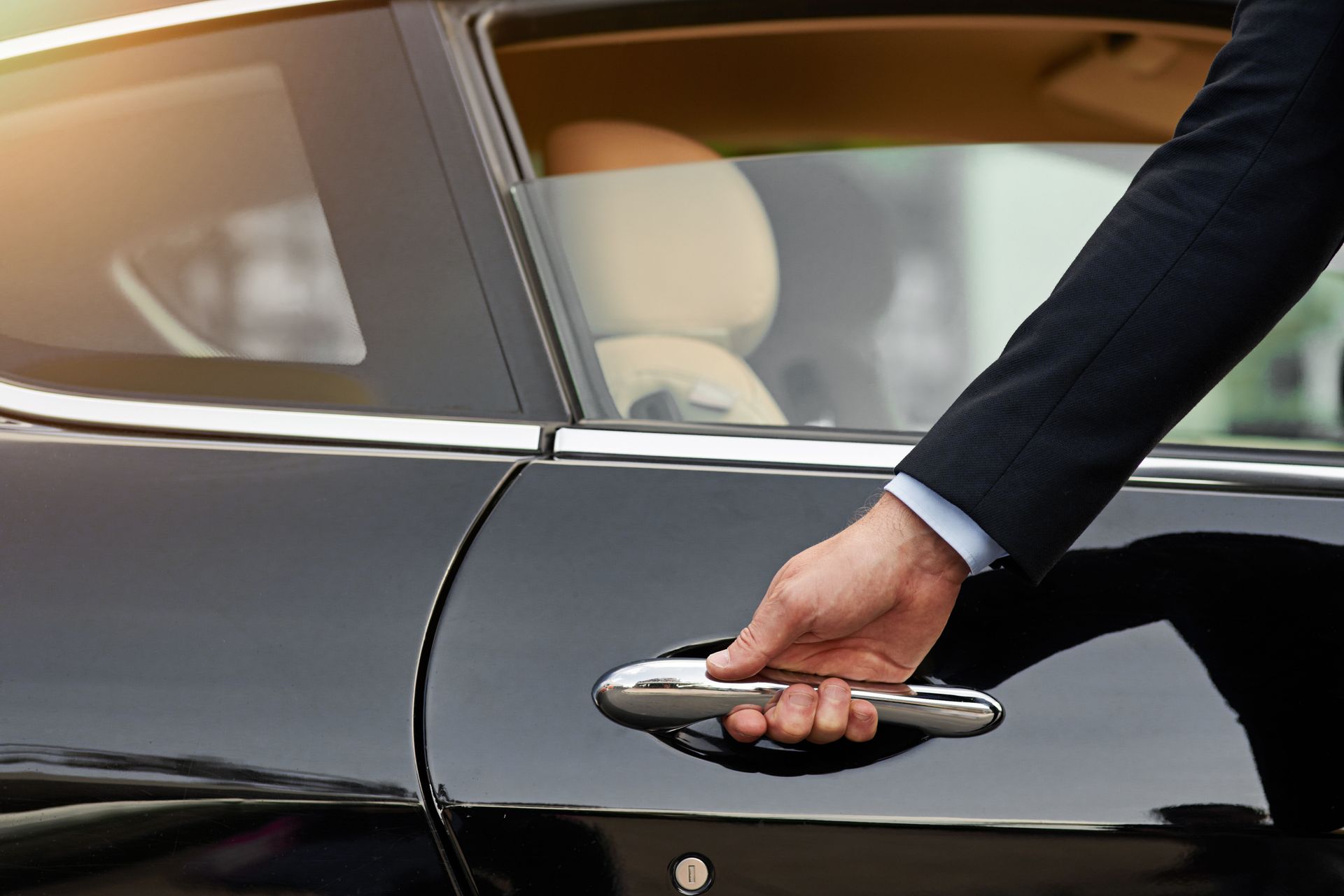 Person in suit opening the door of a black luxury car.