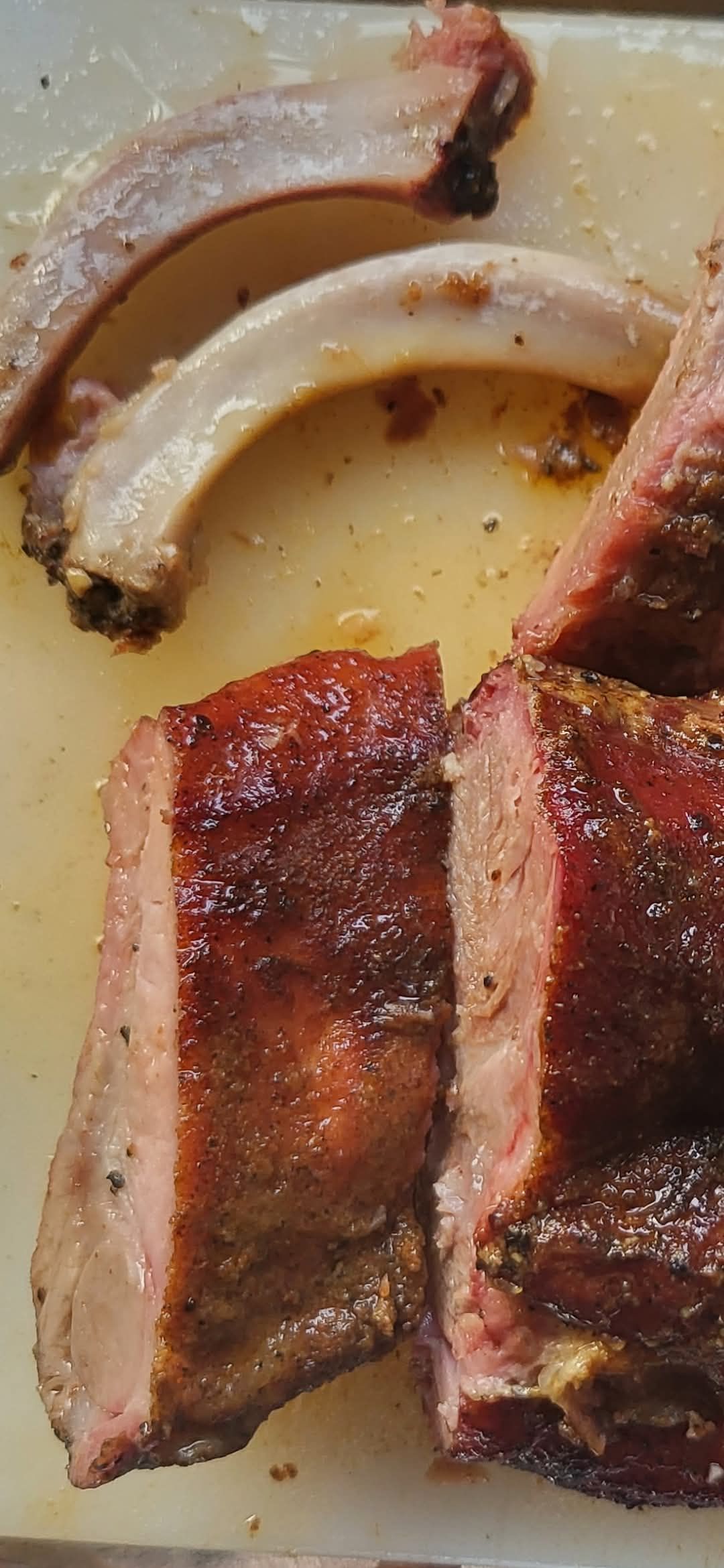 Close-up of sliced, smoked ribs with a dark crust, light-colored bones visible on a cutting board.
