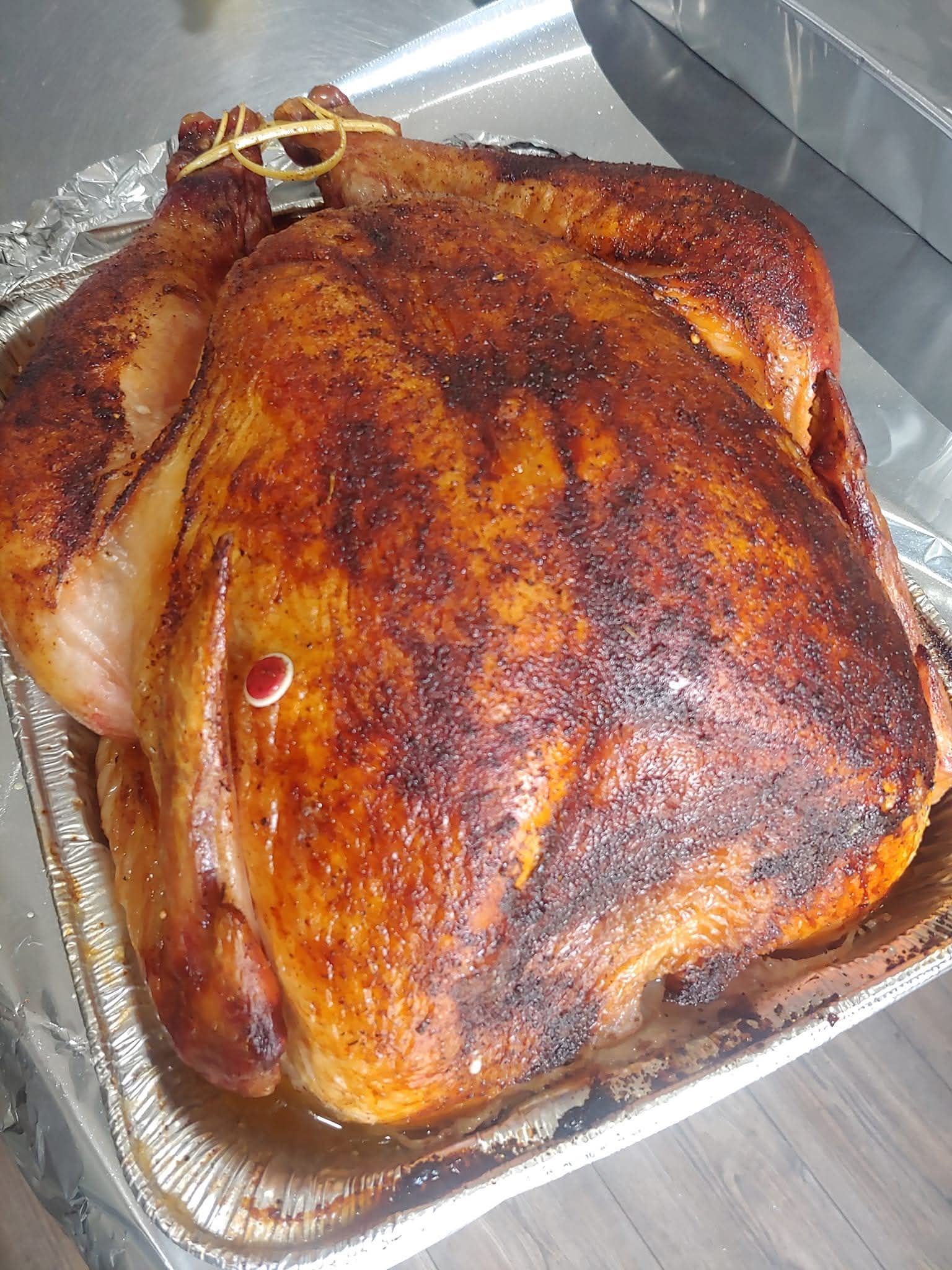 Roasted turkey in a foil pan, with golden-brown skin and a thermometer, ready for serving.