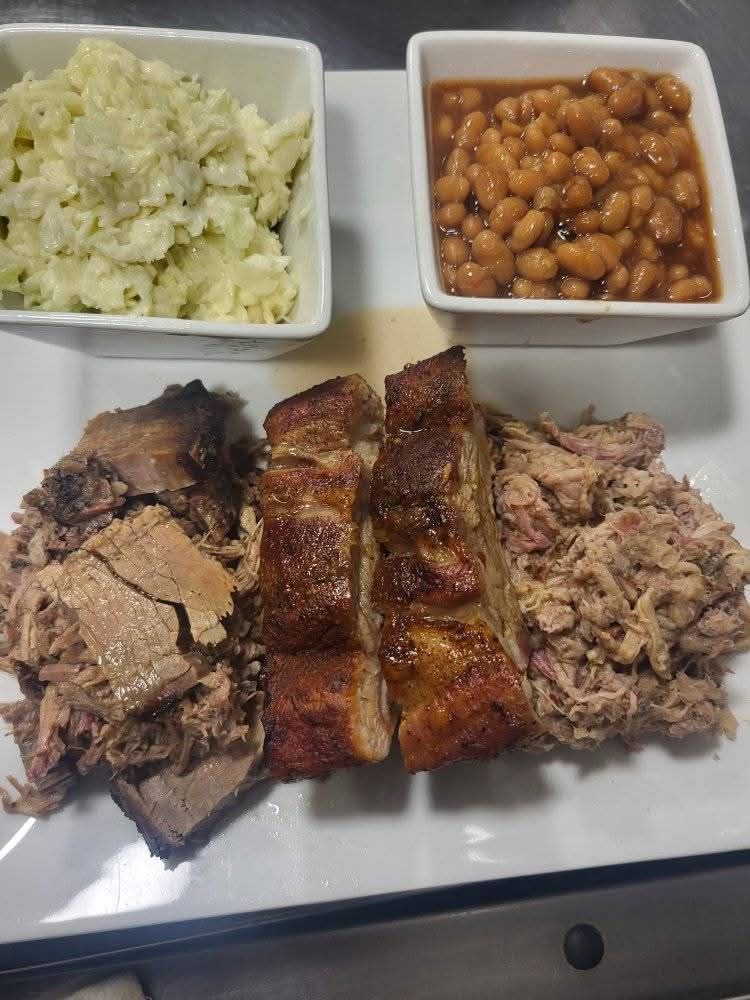 BBQ plate with pulled pork, brisket, ribs, potato salad, and baked beans.