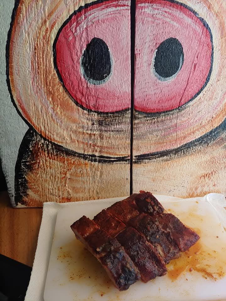 Sliced BBQ ribs on a white cutting board, with a painted pig face in the background.