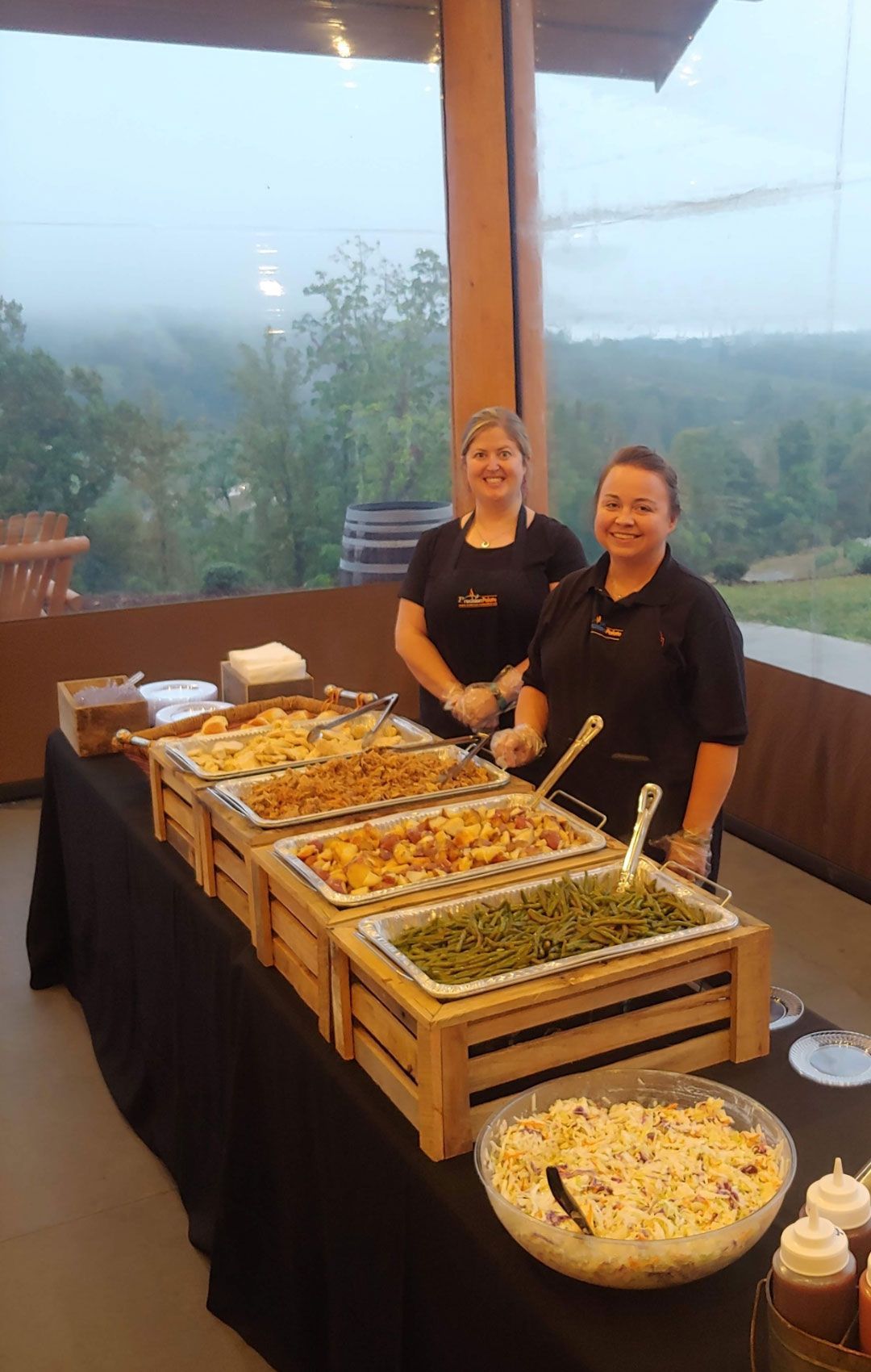 Two caterers behind a buffet table with various dishes outdoors.