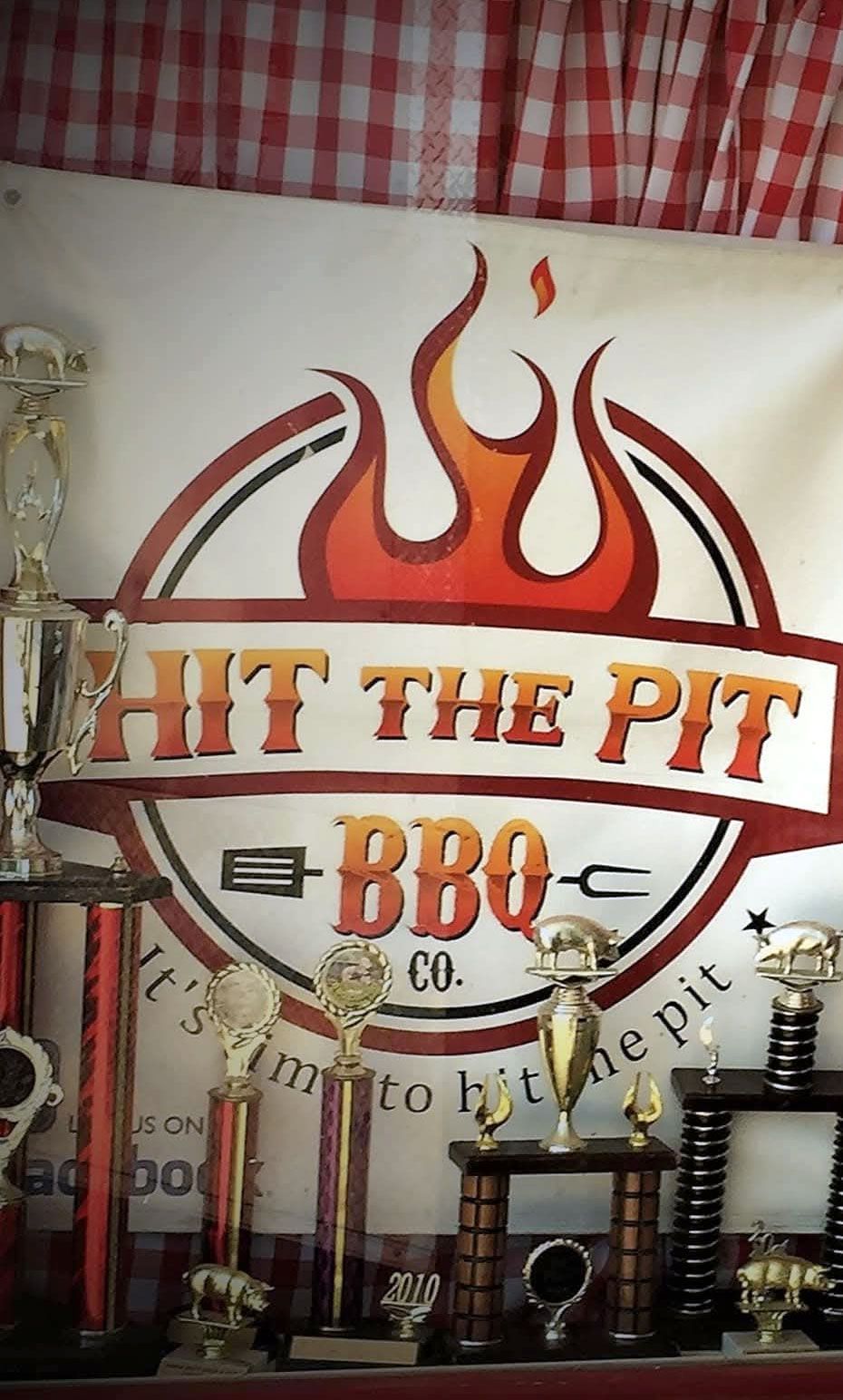 Hit the Pit BBQ Co. logo with flame design, surrounded by trophies, set against a red and white checkered backdrop.