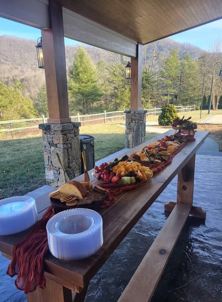 Long wooden table laden with food under a covered patio, mountains in the background.
