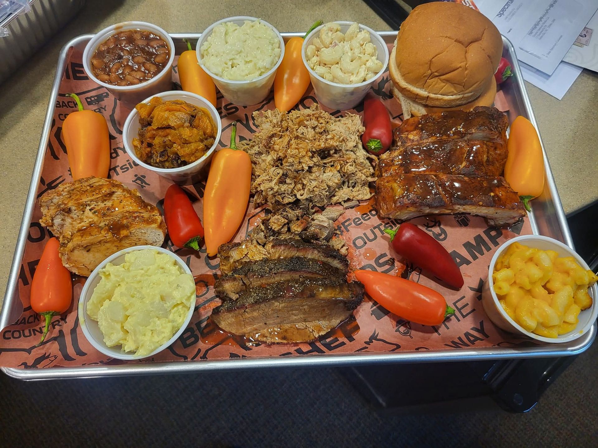 BBQ platter with brisket, ribs, pulled pork, sides, peppers, and a bun.