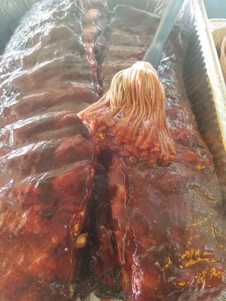 Rack of barbecued ribs with sauce being applied.