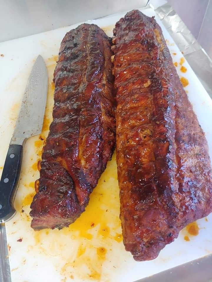 Two racks of barbecued ribs on a white cutting board next to a knife.