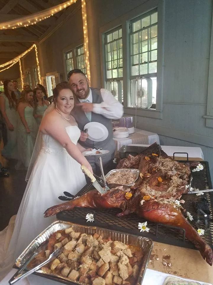 Bride and groom cutting roasted pig at wedding reception. Guests in background. Festive decorations.