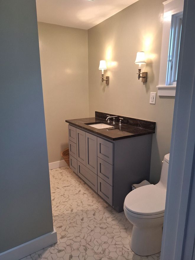 Bathroom with gray vanity, black countertop, white toilet, and sconce lighting.