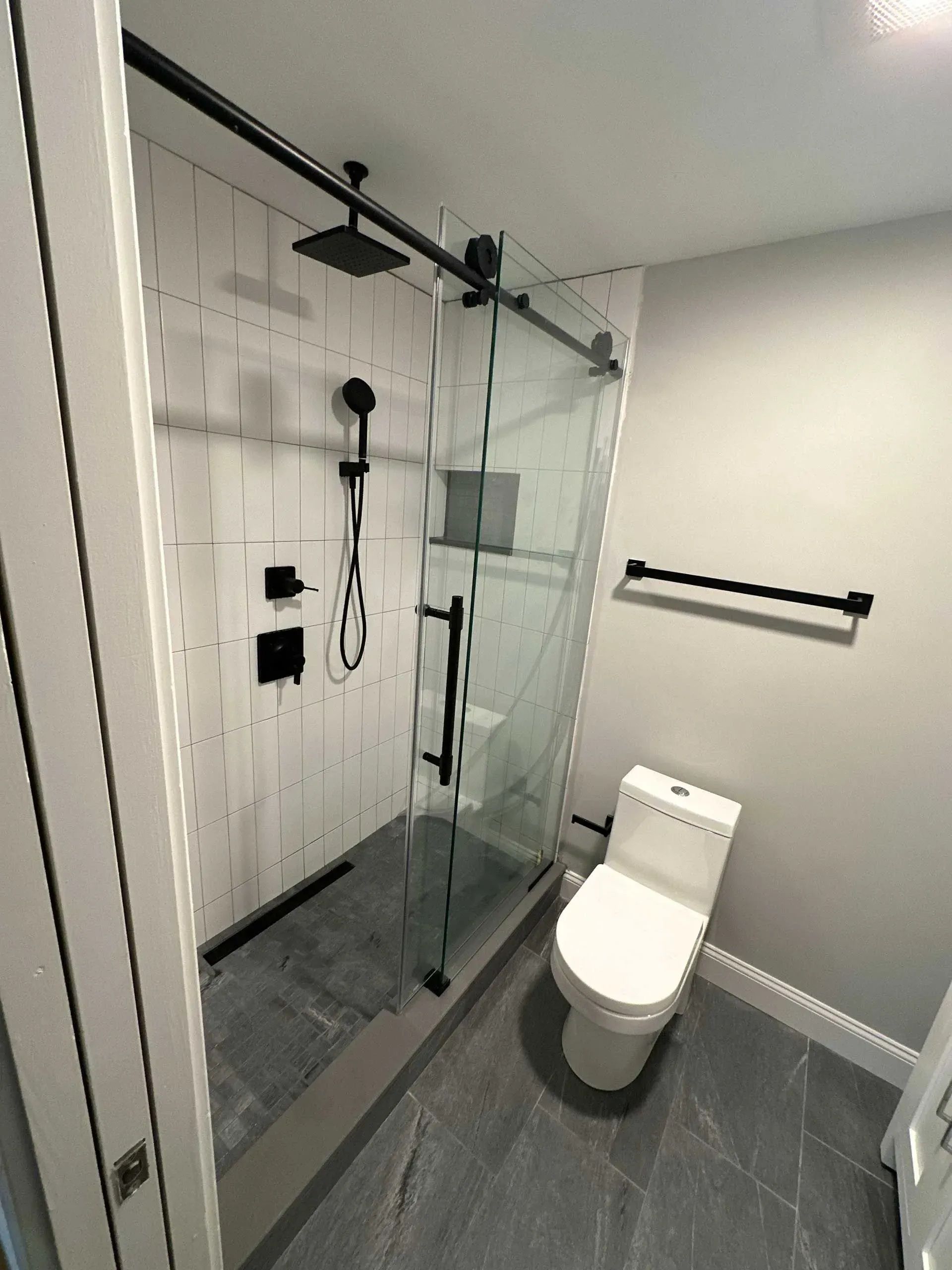 Modern bathroom with glass shower, black fixtures, white vertical tile, and a toilet.