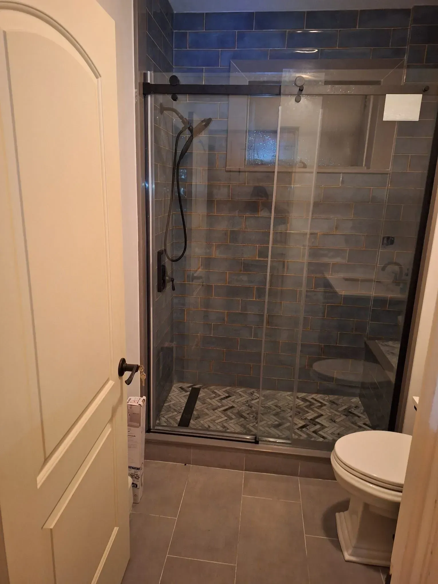 Bathroom with a glass shower, dark tile walls, and a white toilet.