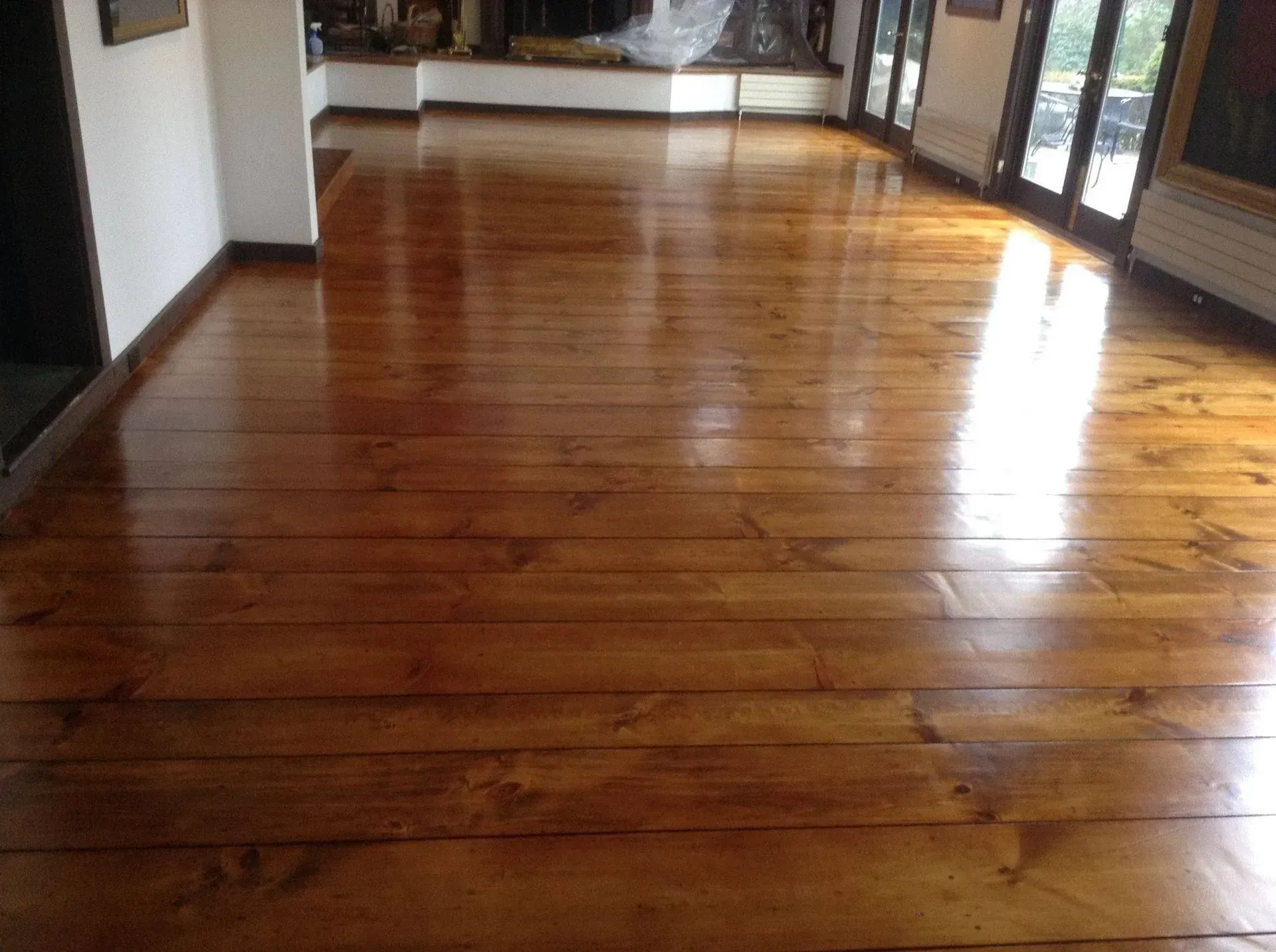 Glossy wooden floor in a sunlit room, with dark wood trim along the walls.
