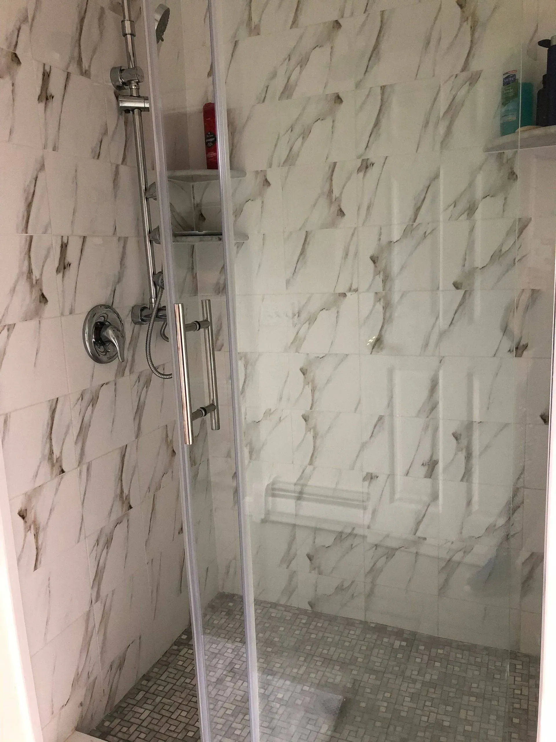 Shower with white and gray marble-look tile, glass door, and pebble floor.