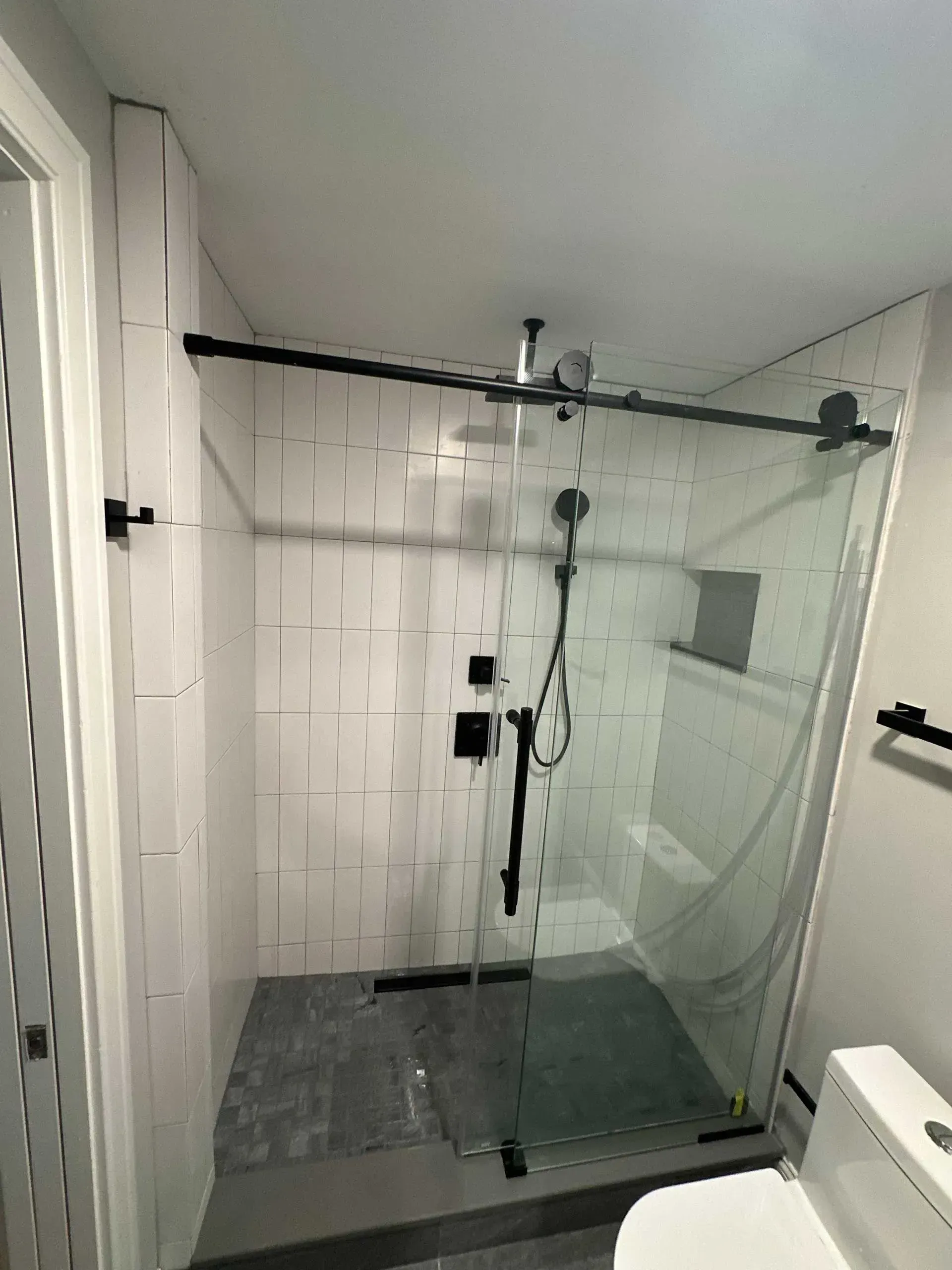 Modern bathroom with glass shower door, black fixtures, white tile, and a toilet.