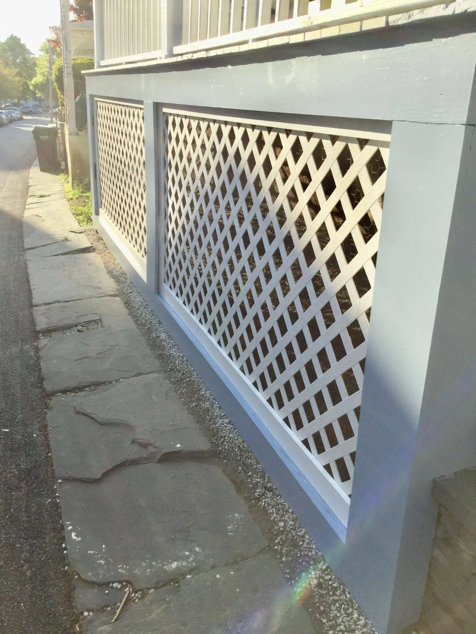 Gray house foundation with white lattice panels, blue trim, and stone sidewalk.