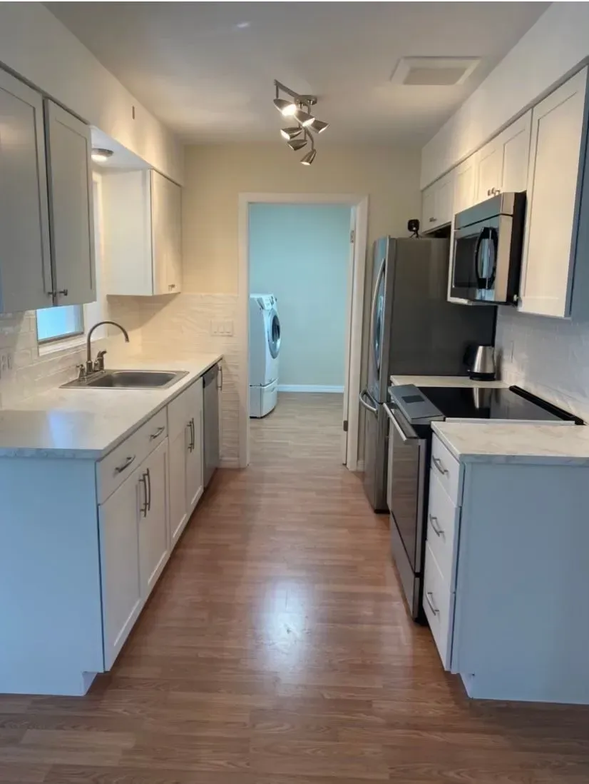 Kitchen with white cabinets, stainless steel appliances, and wood flooring, leading to a laundry area.