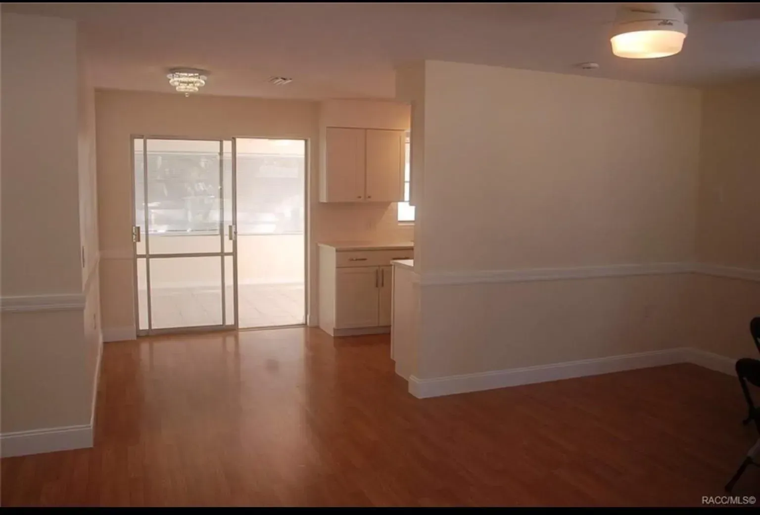 Empty interior with sliding door to outside, light-colored walls, wood floors, and kitchen cabinets.
