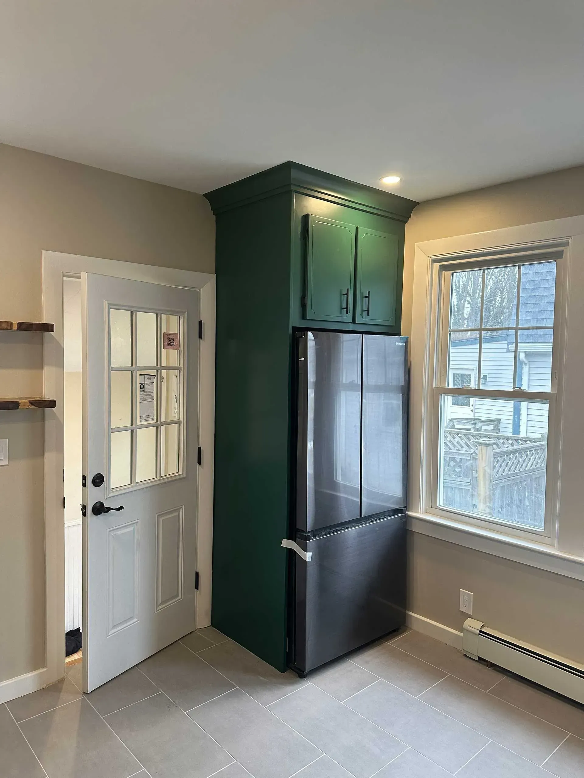 Green cabinet, refrigerator, and doorway in a kitchen corner. Window on the right.