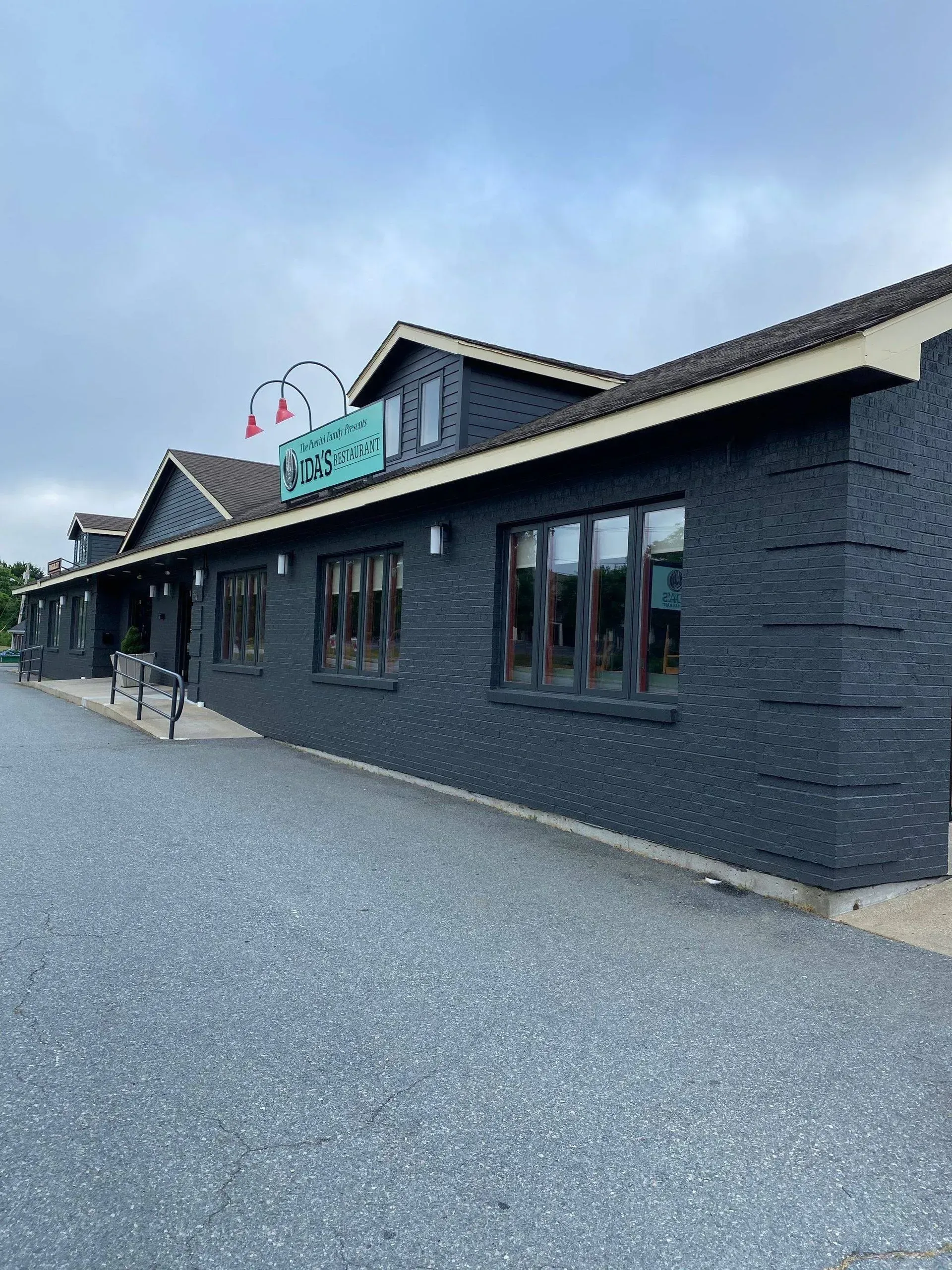 Dark gray brick building with sign "Restaurant & Bar". Gray gravel parking. Overcast sky.
