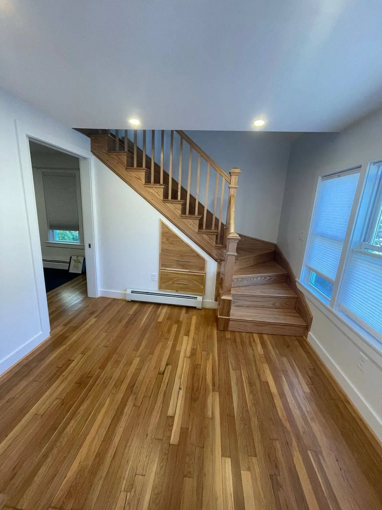 Interior view of a house with wooden floors, stairs, and a window.