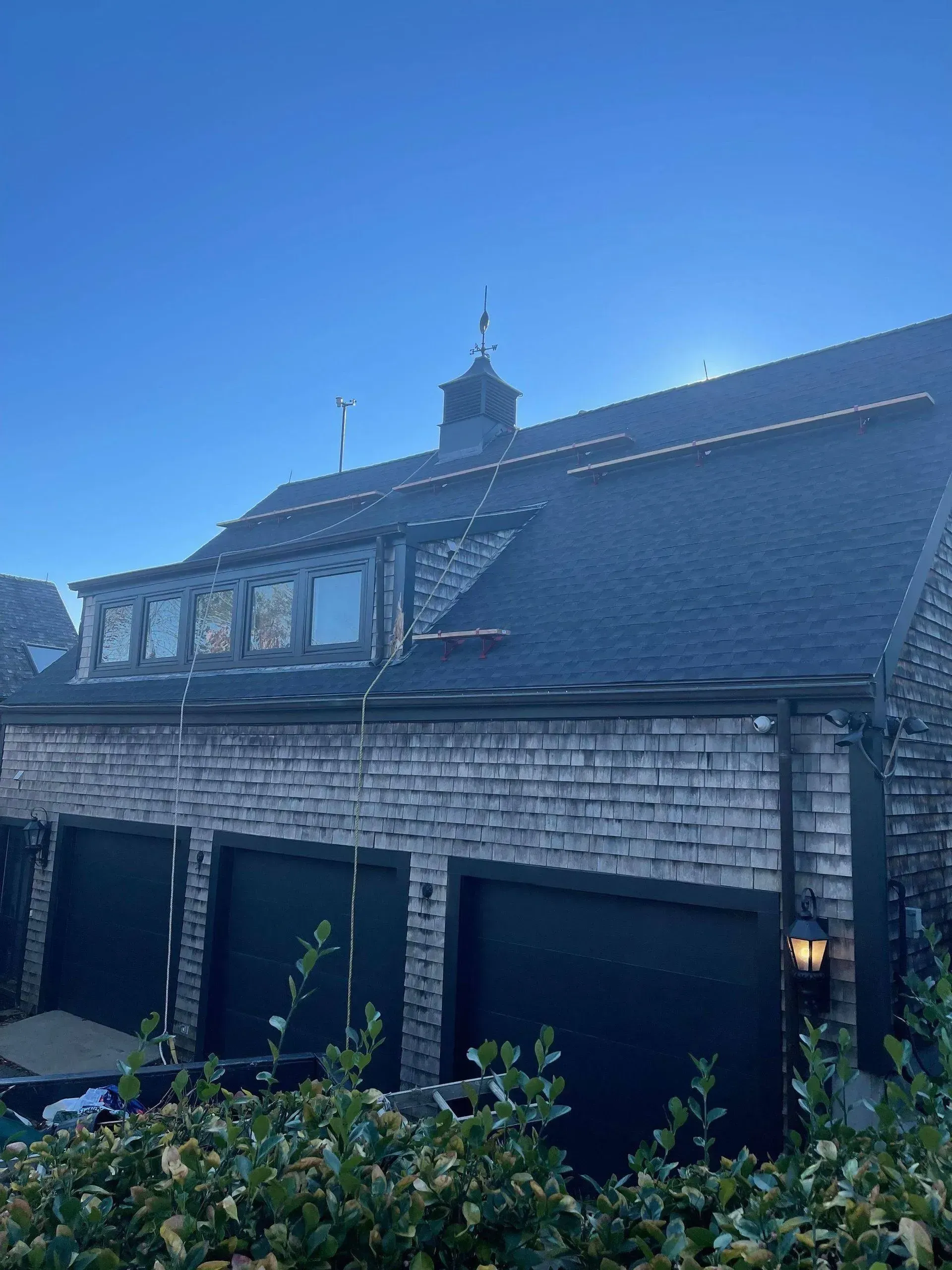 Gray shingled building with three garage doors. Dormers with windows and a cupola on roof.