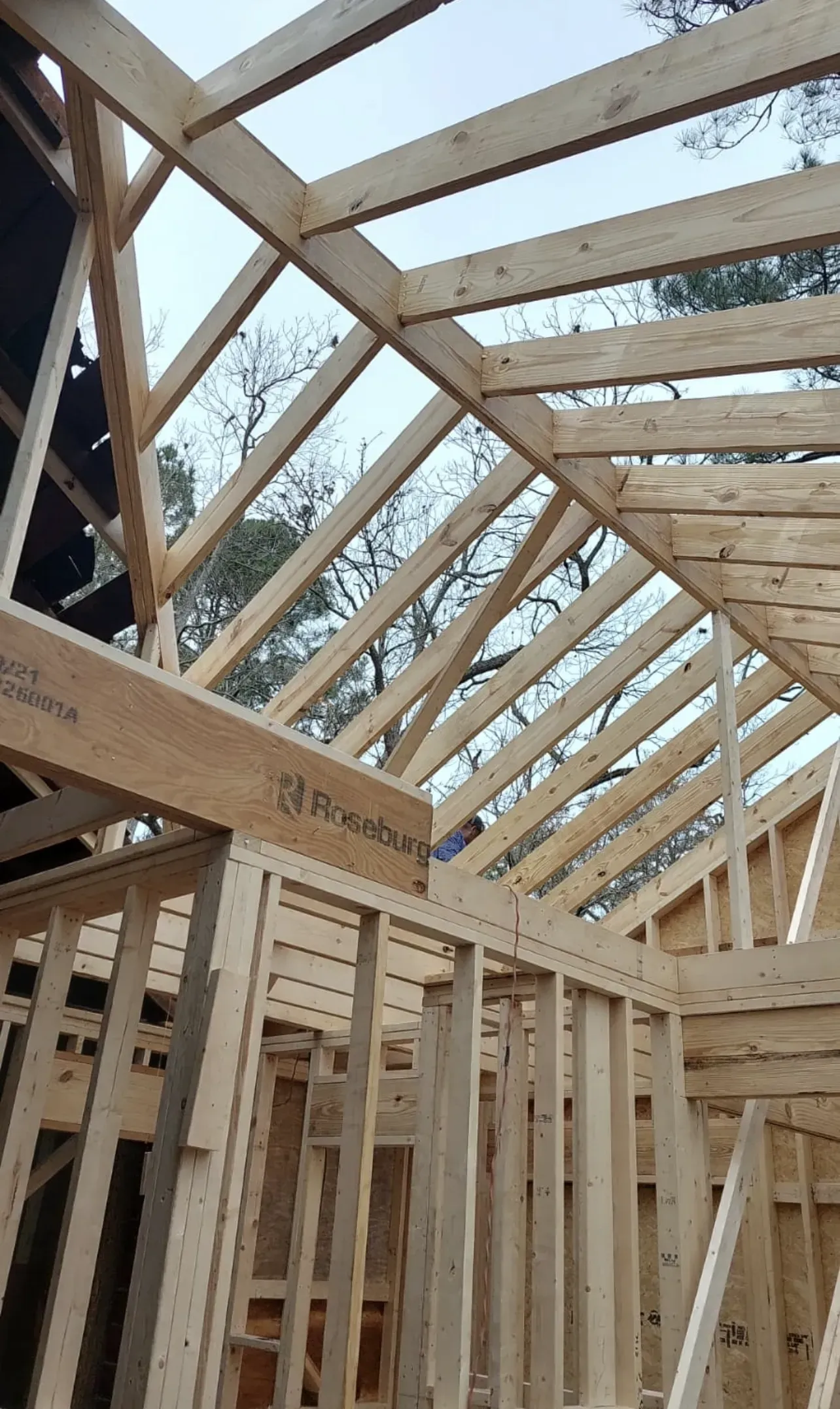 Wooden house framing under construction, exposed beams, natural wood color, outdoor setting.