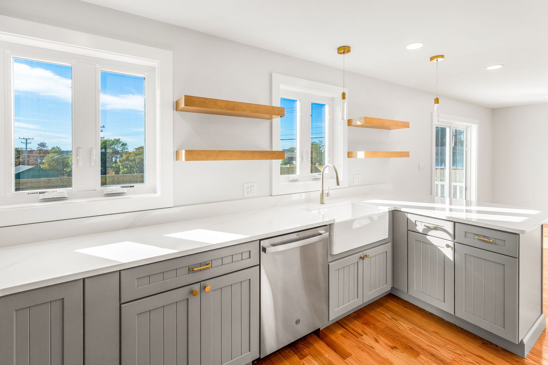 Modern kitchen with gray cabinets, white countertops, and wood shelves. Large windows offer a view.