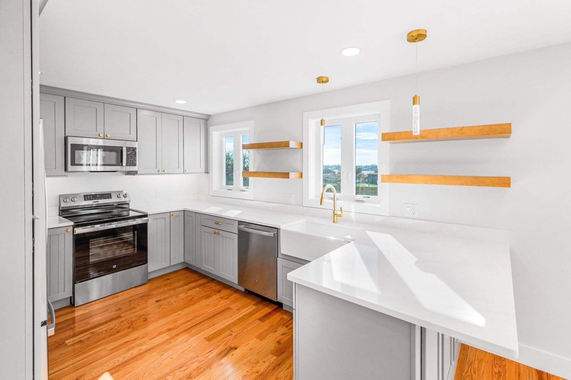 Light gray kitchen with stainless steel appliances, wooden shelves, and white countertops.
