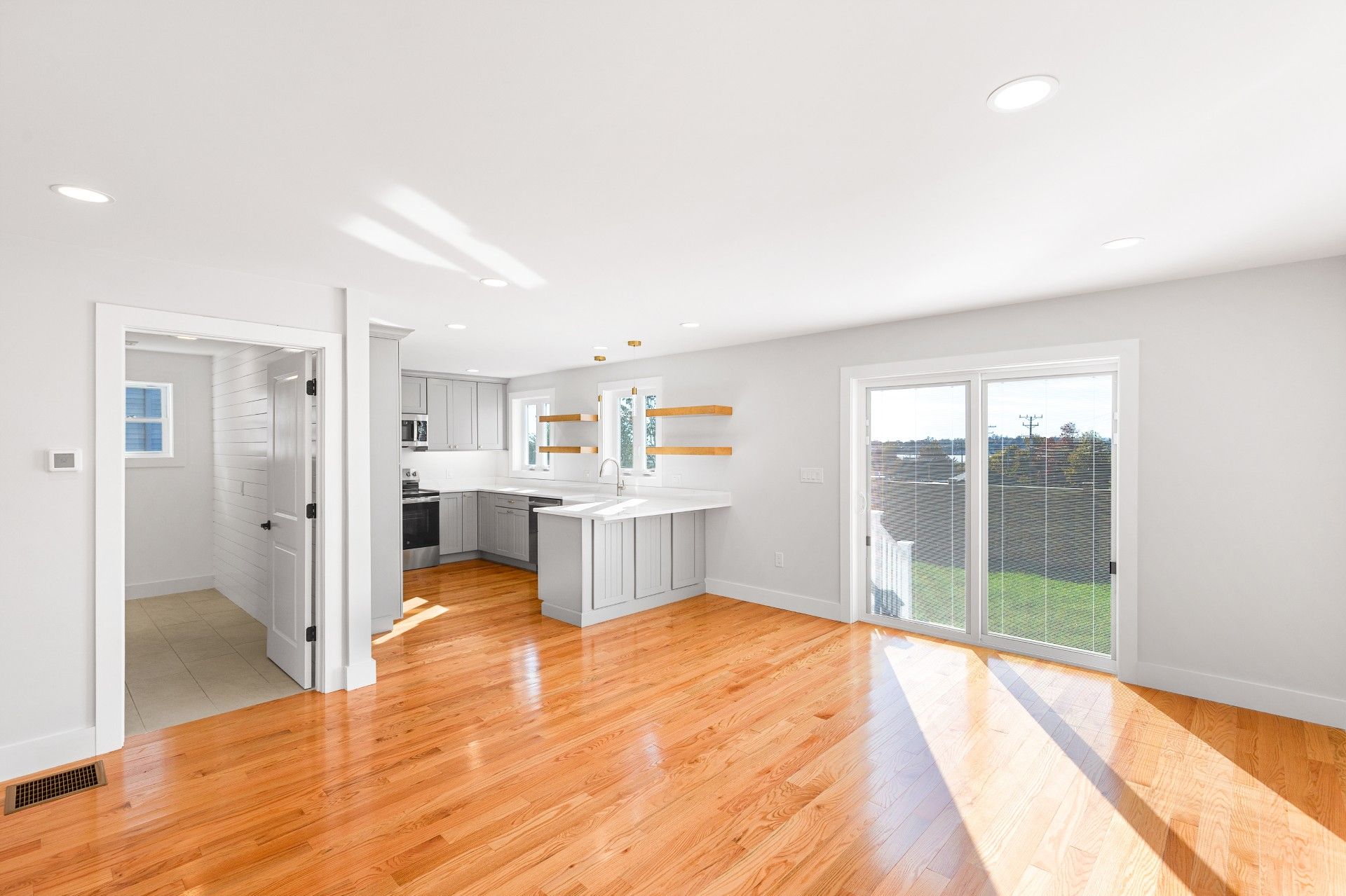 Bright, open-concept living space with hardwood floors, kitchen, and sliding glass door.