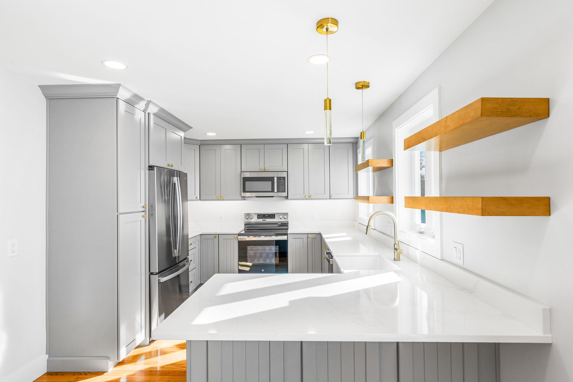 Gray and white kitchen with stainless steel appliances, white countertops, and wooden shelves.