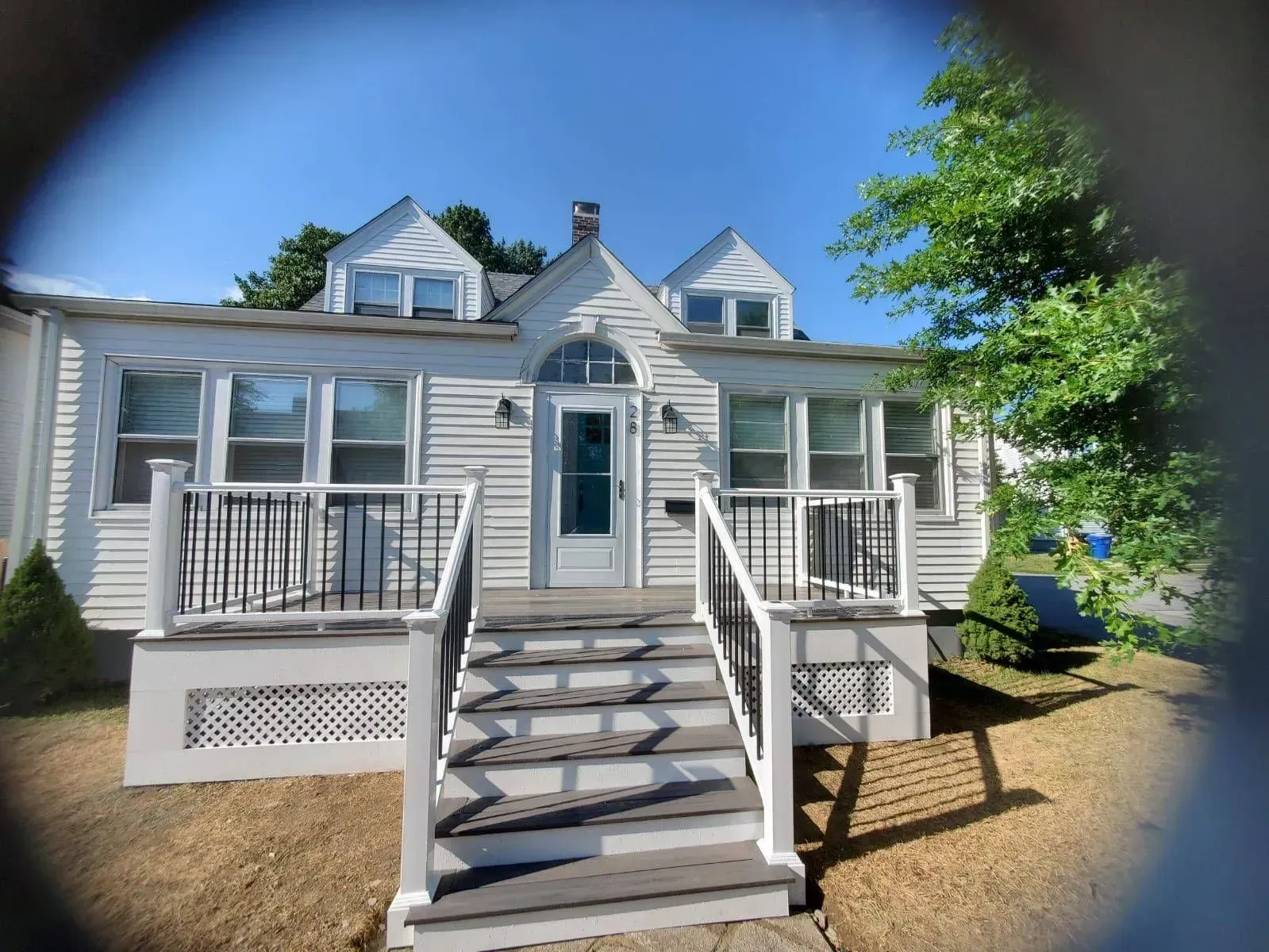 White house with black railing porch and steps, blue sky.