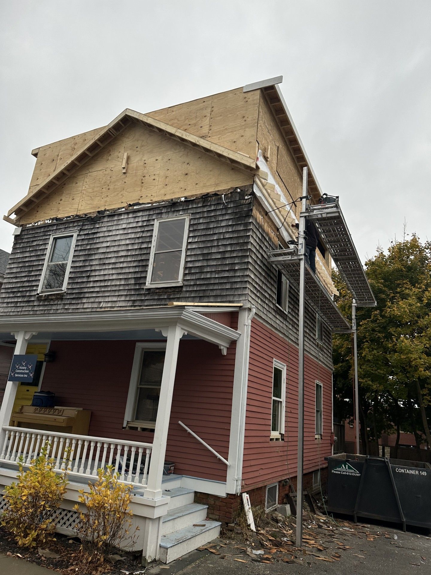 A multi-story house undergoing roof renovation. Scaffolding is set up; the roof is partially rebuilt with new plywood.