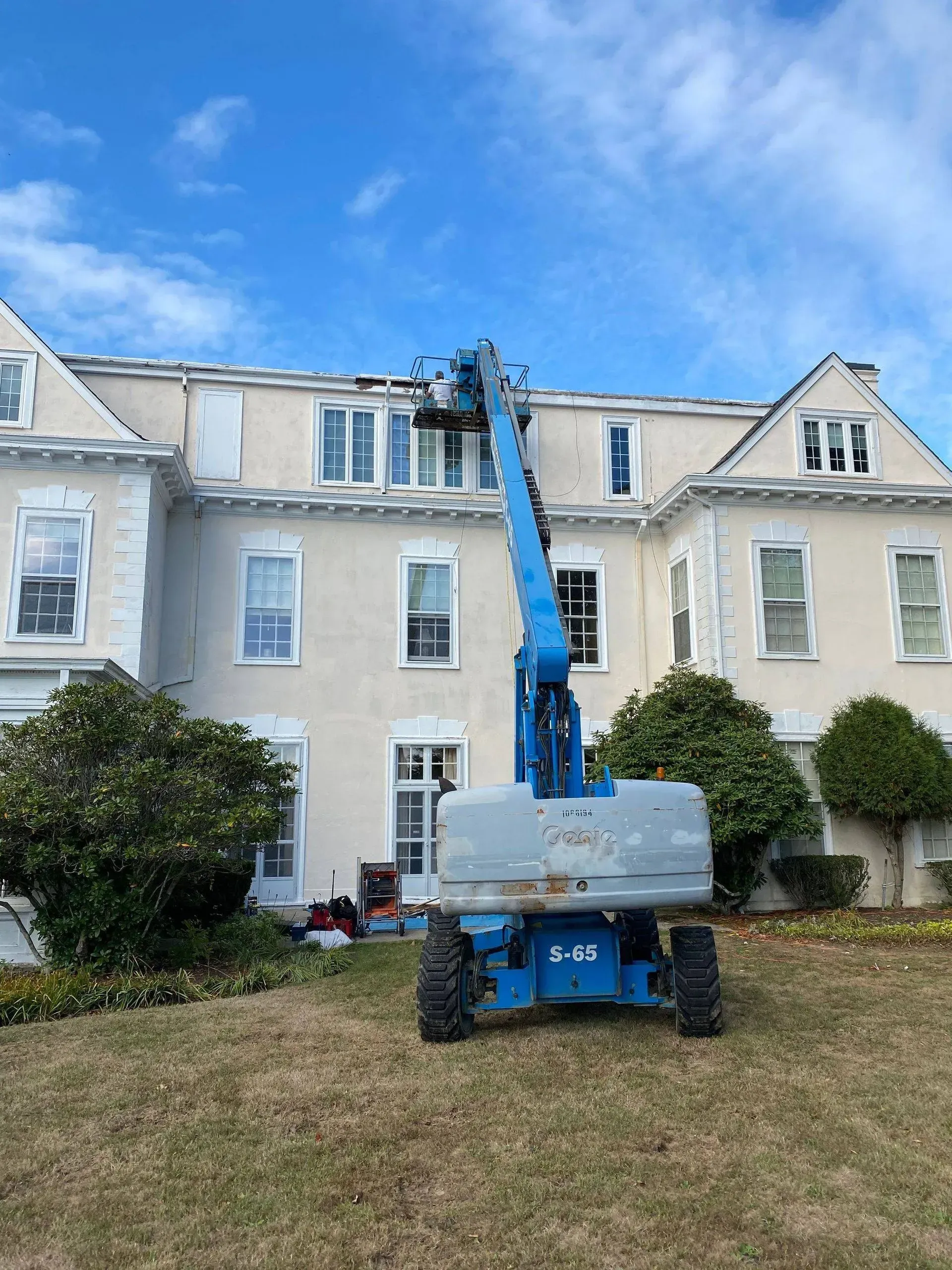 Blue lift servicing roof of a light-colored building under a blue sky.