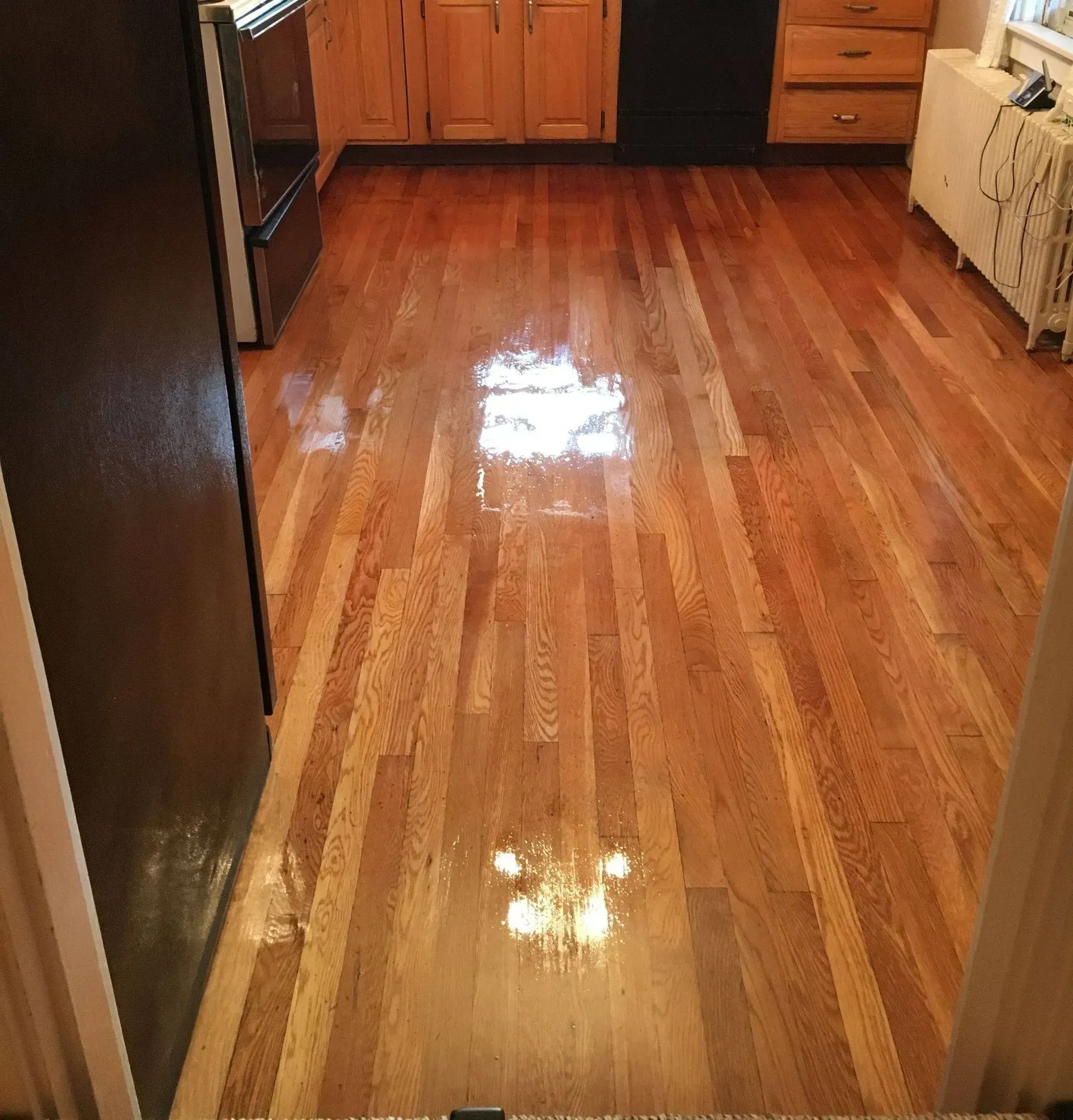Wooden floor in a kitchen with brown cabinets and a black refrigerator.