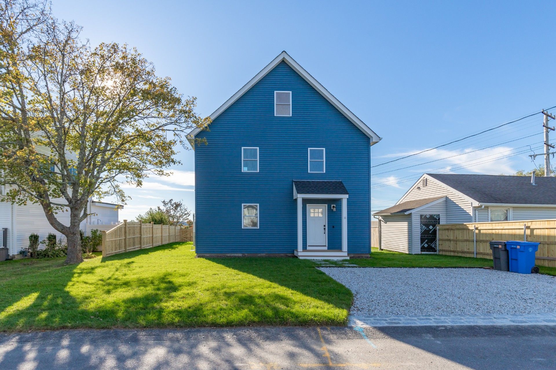 Tan shed with black roof, in a grassy area with trees and blue sky.