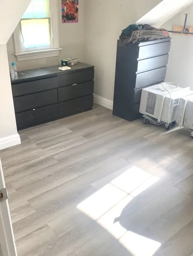 a room with hardwood floors, a dresser, and a window