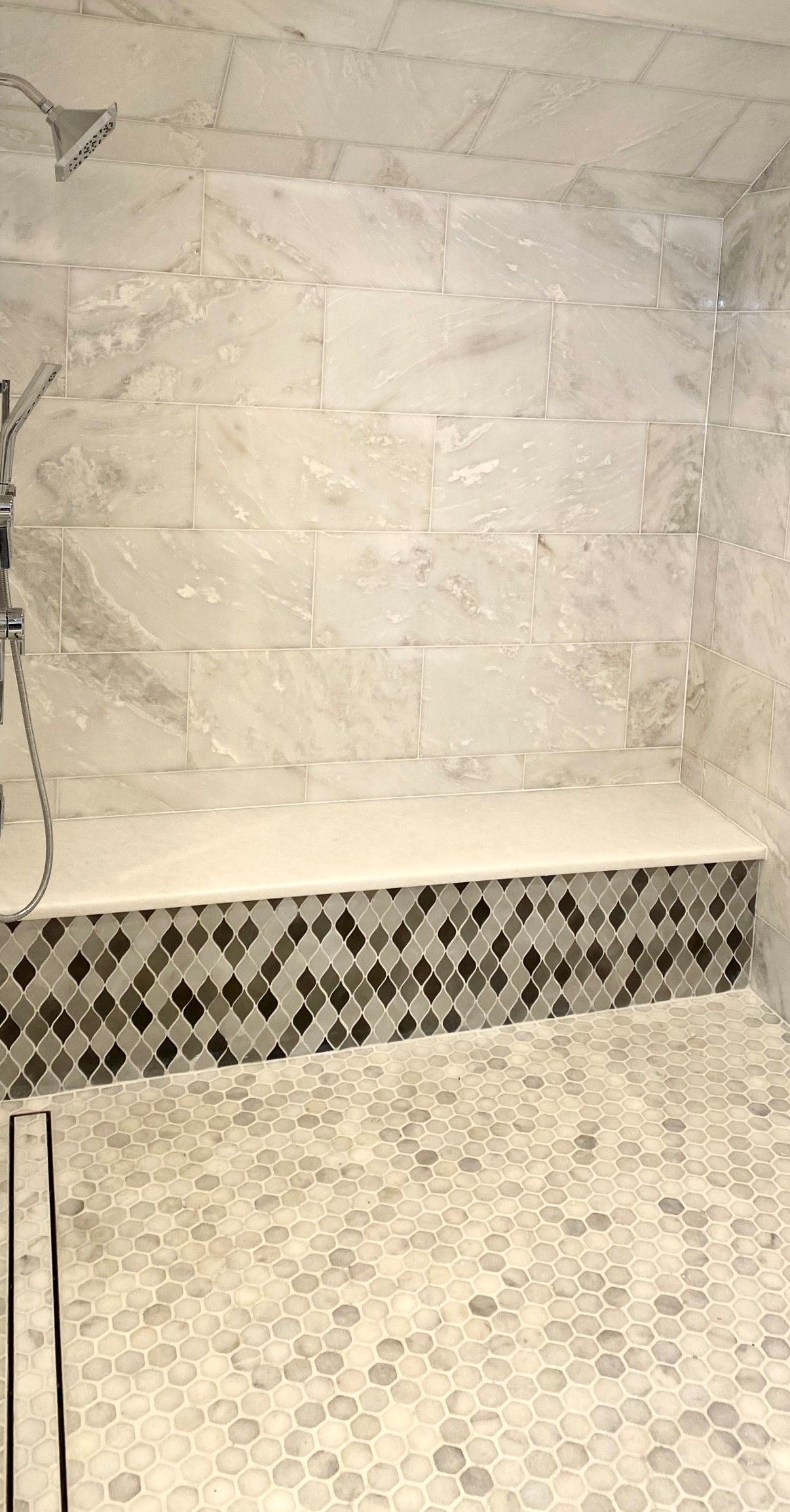 A walk in shower with a bench and a shower head.