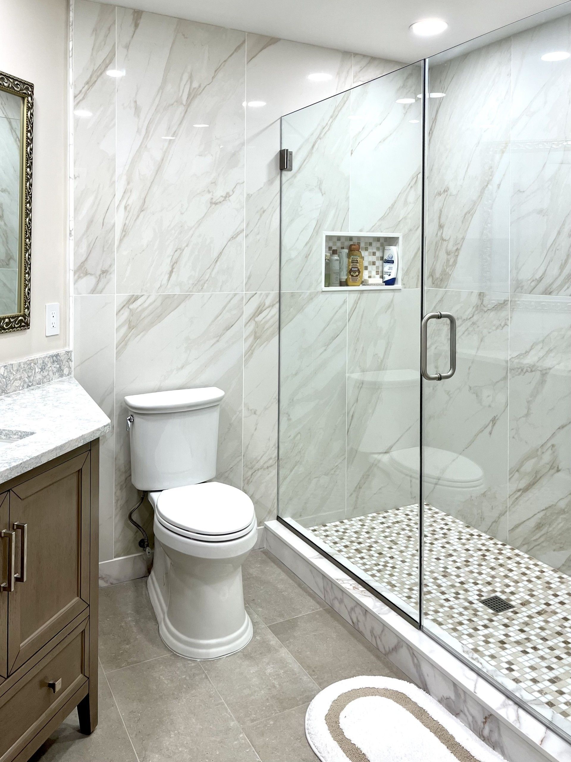 Bathroom with marble-look tile, glass shower, pebble floor, vanity, and toilet.