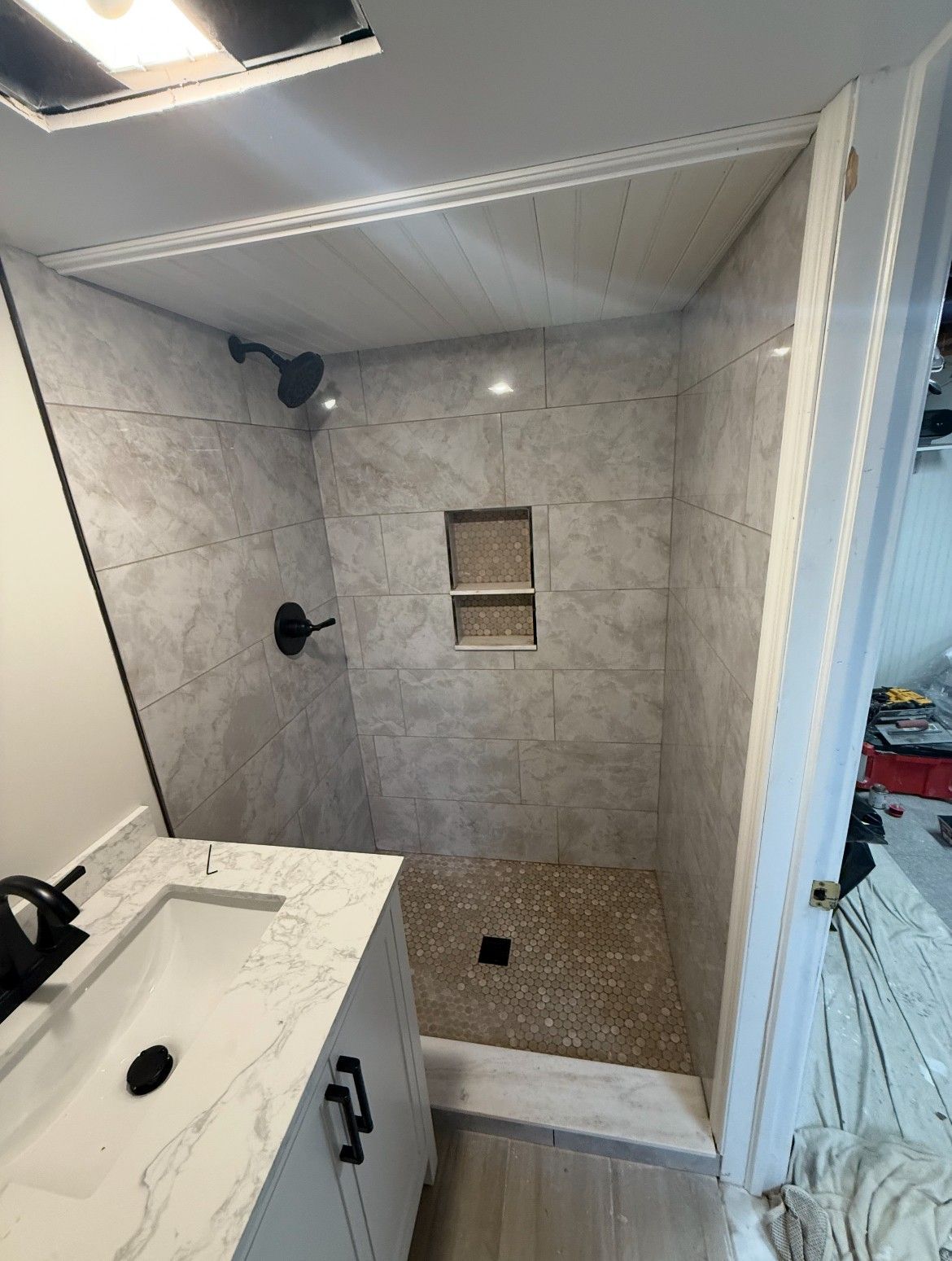 Newly renovated shower with gray tile walls, pebble floor, and black fixtures.