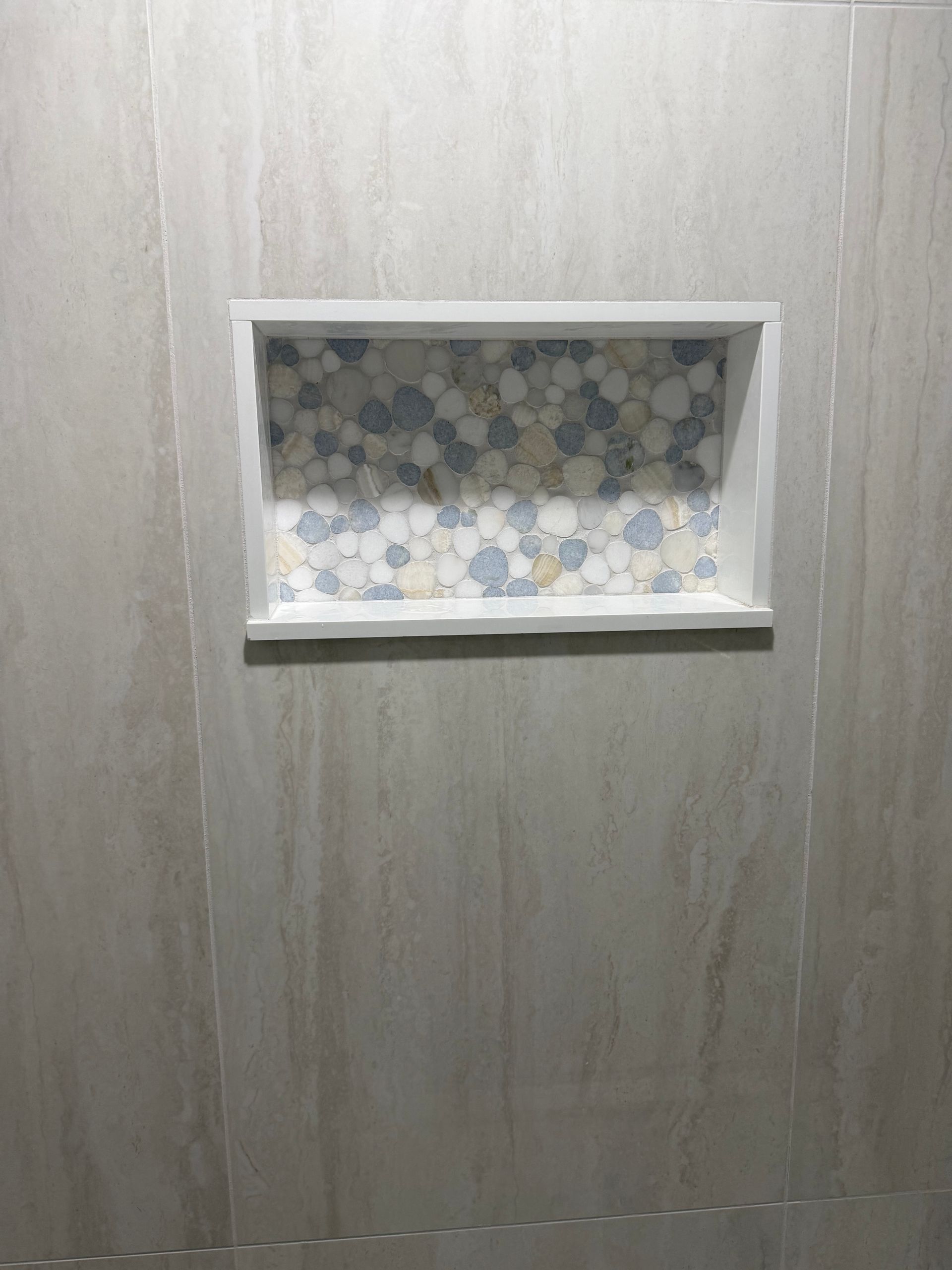 A shower niche in a bathroom with a mosaic tile design.