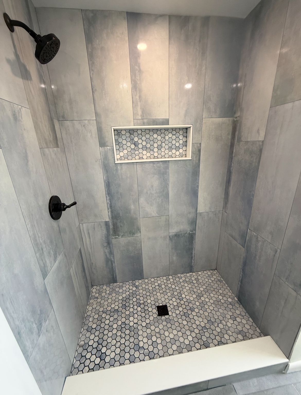 Shower with blue and gray tile, dark fixtures, and a built-in shelf.