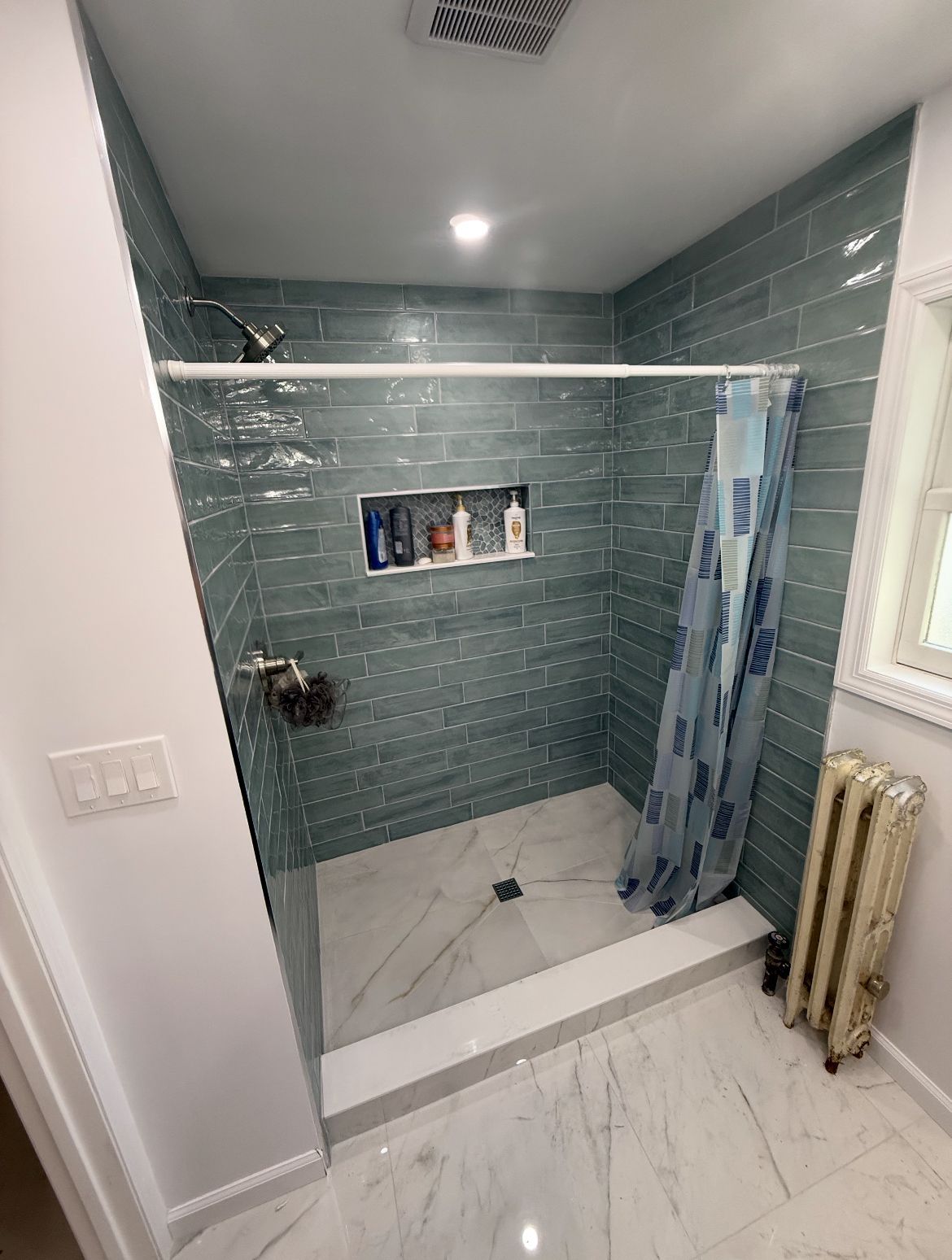 Modern bathroom with teal tiled shower, marble floor, and radiator.