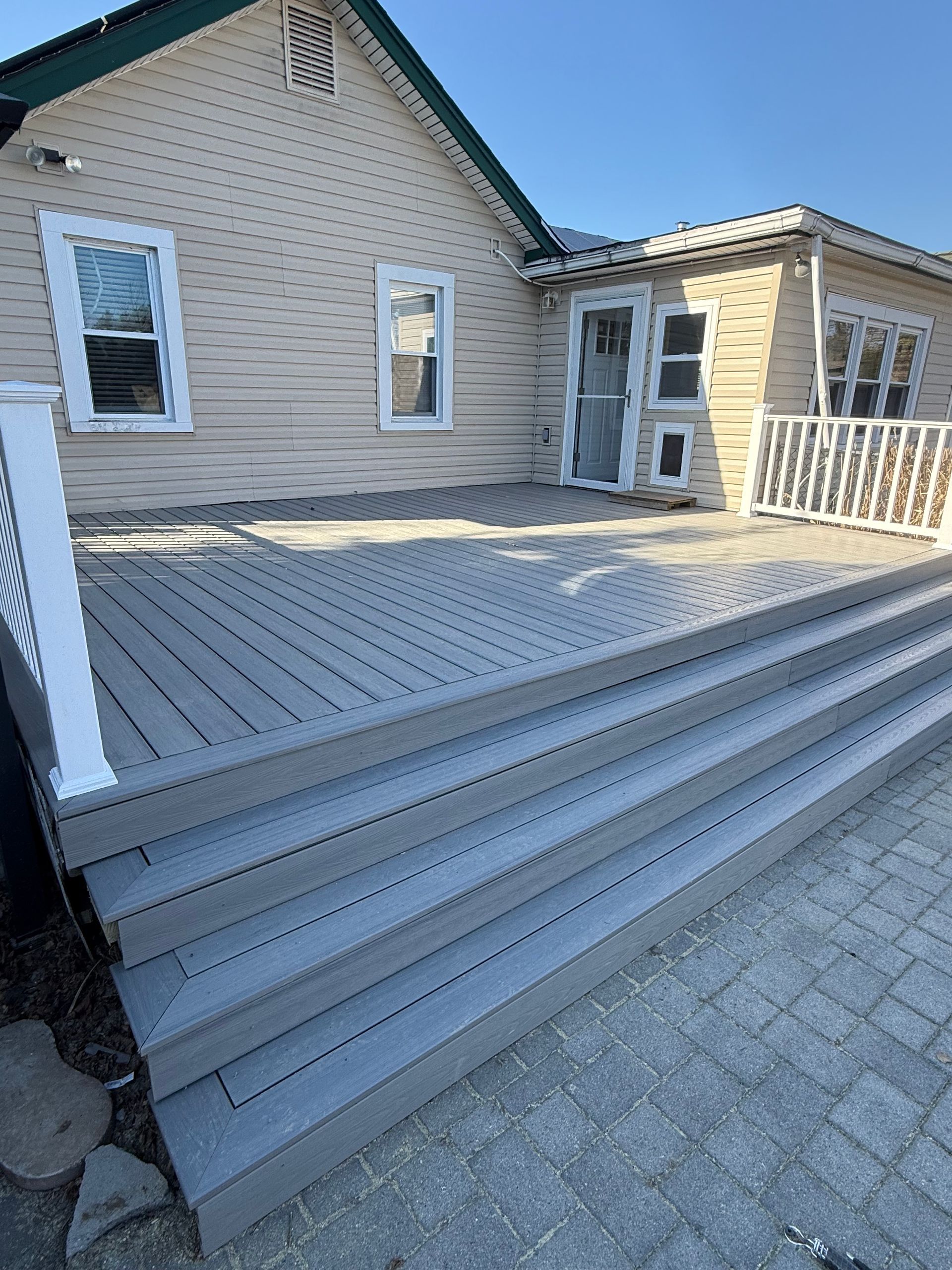 A gray deck with stairs and a white railing in front of a house.