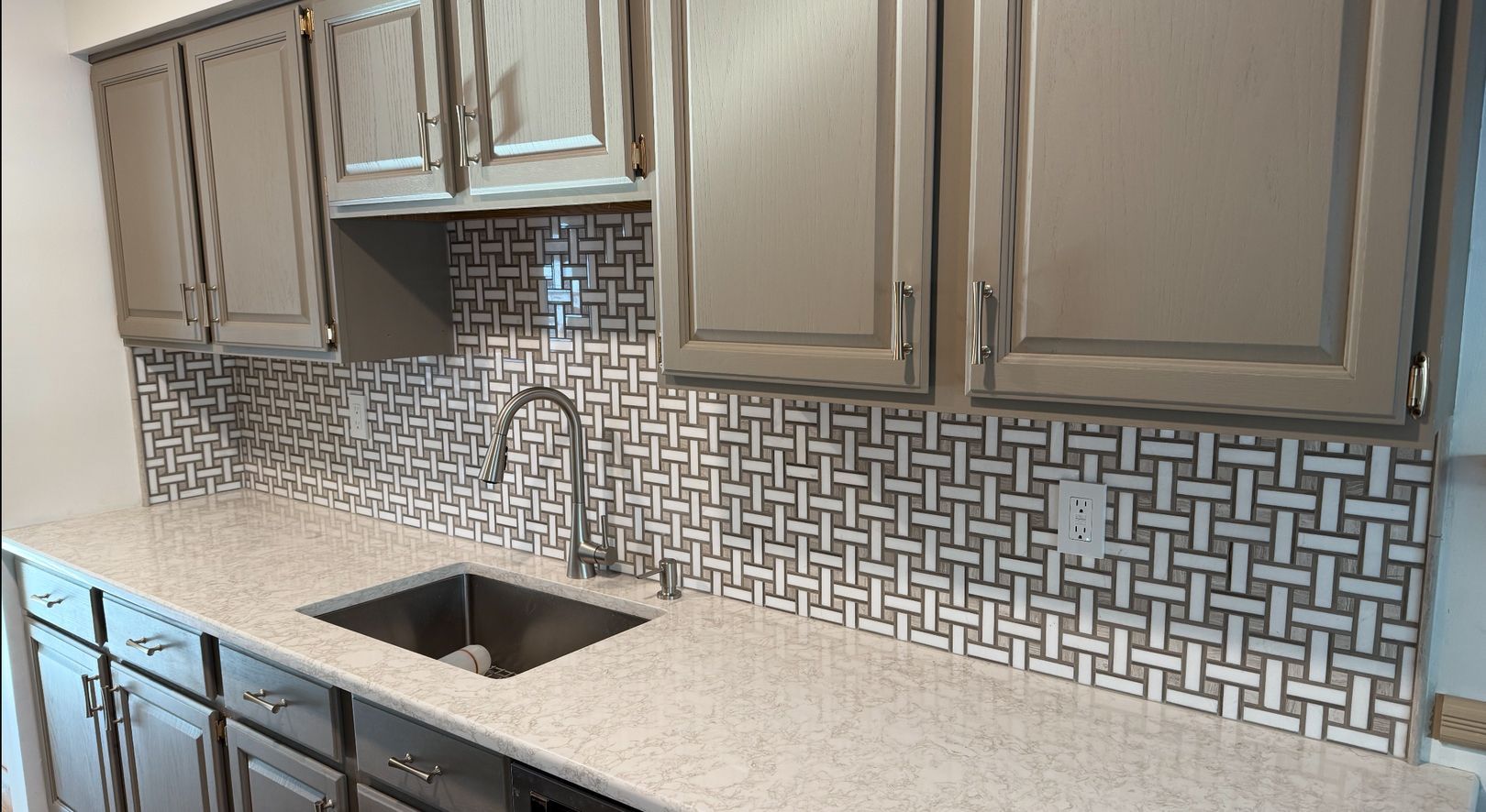 A kitchen with gray cabinets and a stainless steel sink.